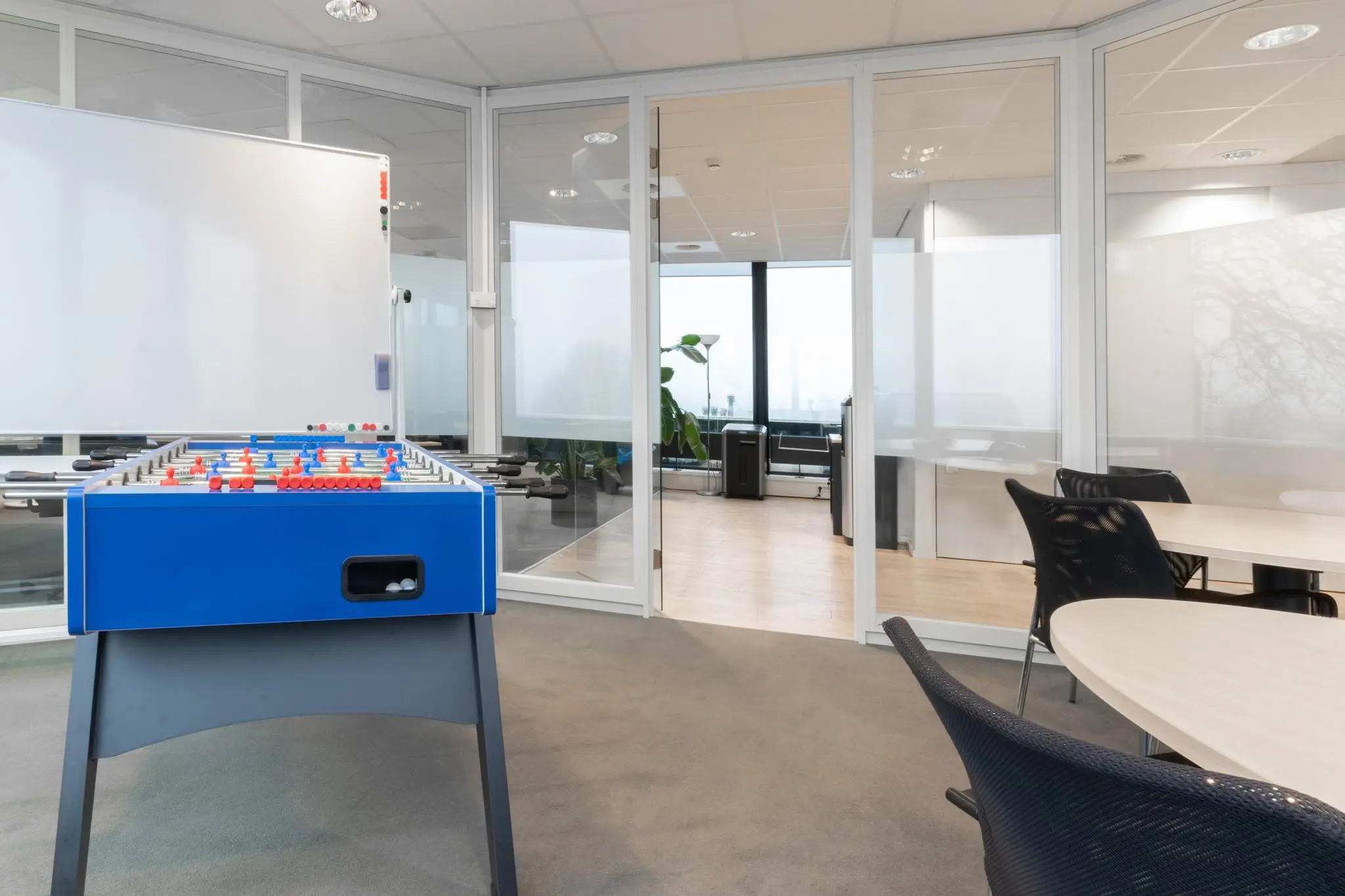 Moderne kantoorruimte aan de 1e Hogeweg met glazen wanden, een tafelvoetbaltafel en vergadertafels.